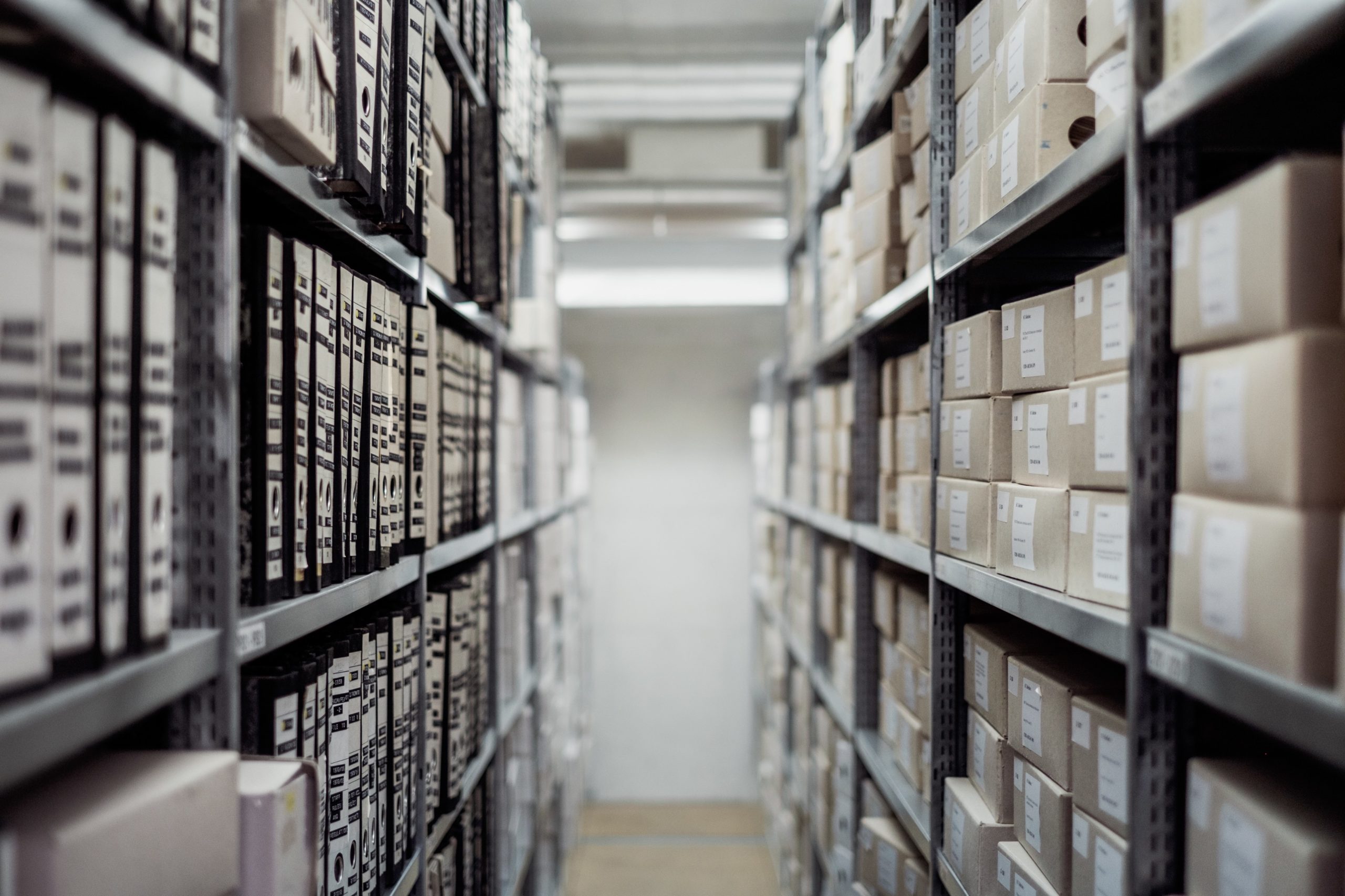 Photo of documents in a lane of shelves in an archive by Samuel Zeller/Unsplash